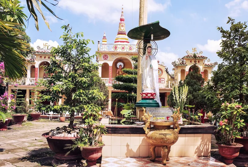 Tượng Quan Âm trắng đứng giữa cây cảnh trong khuôn viên chùa Tiên Châu ở An Bình, Vĩnh Long.