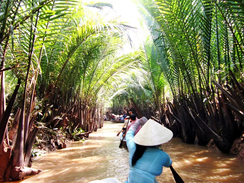 Người chèo đội nón lá đưa thuyền qua con rạch nhỏ rợp bóng dừa nước ở Đồng bằng sông Cửu Long.