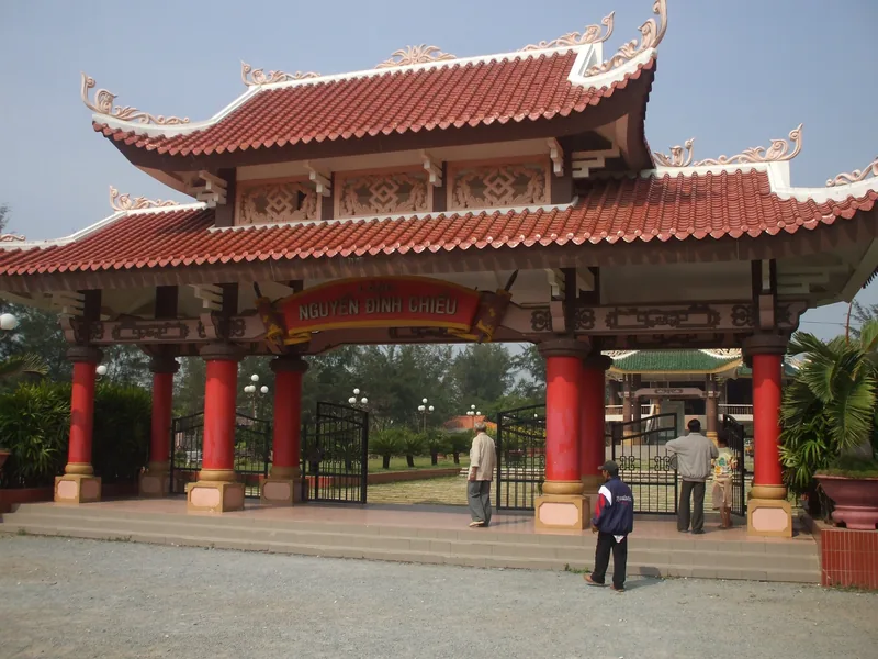 Cổng tam quan mái đỏ nhiều tầng dẫn vào khu di tích Nguyễn Đình Chiểu ở đồng bằng sông Cửu Long.