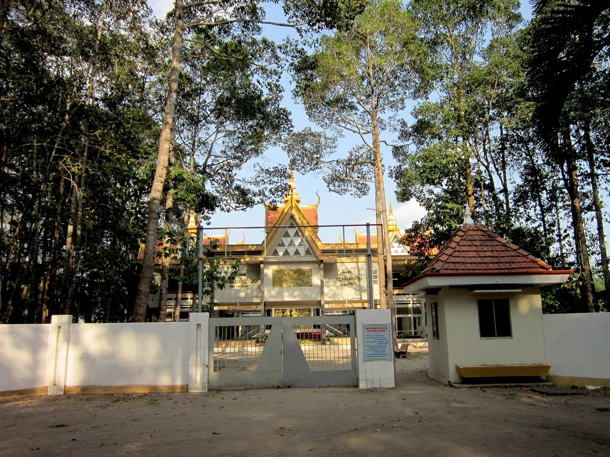 Ngôi chùa Khmer với mái nhọn tinh xảo nằm sau cổng tường bao, xung quanh là hàng cây cao ở Trà Vinh.