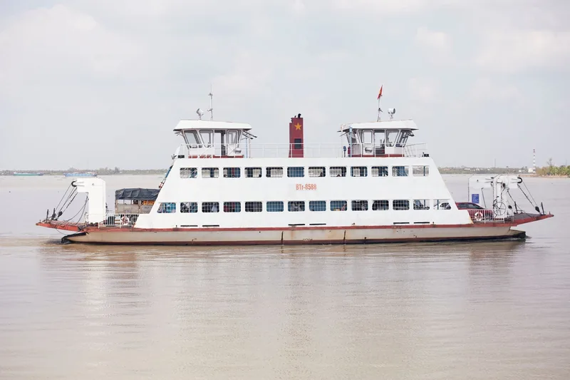 Chiếc phà hai đầu chở xe và người, mang cờ Việt Nam, băng qua dòng sông rộng ở Đồng bằng sông Cửu Long.