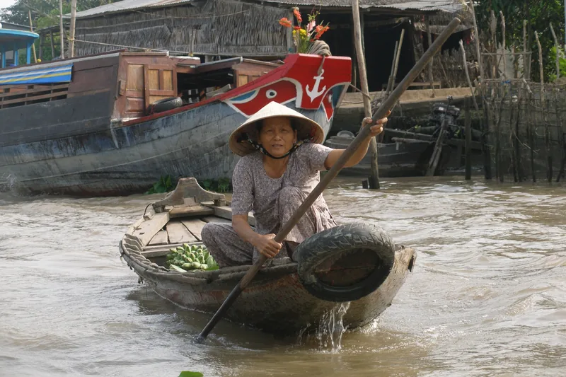 Một người phụ nữ đội nón lá chèo thuyền gỗ nhỏ chở nông sản tại chợ nổi ở đồng bằng sông Mekong.