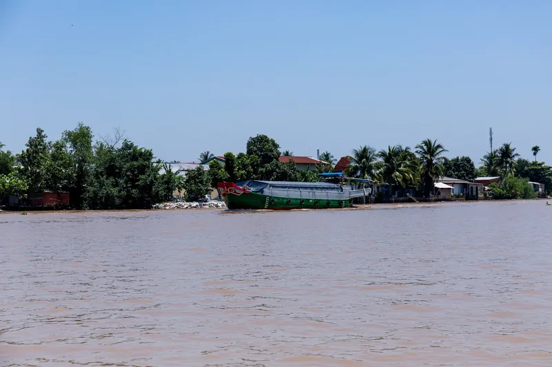 Một sà lan chở hàng nằm bên bờ sông đầy bùn với hàng cây dừa ở Đồng bằng sông Mekong gần Bến Tre.