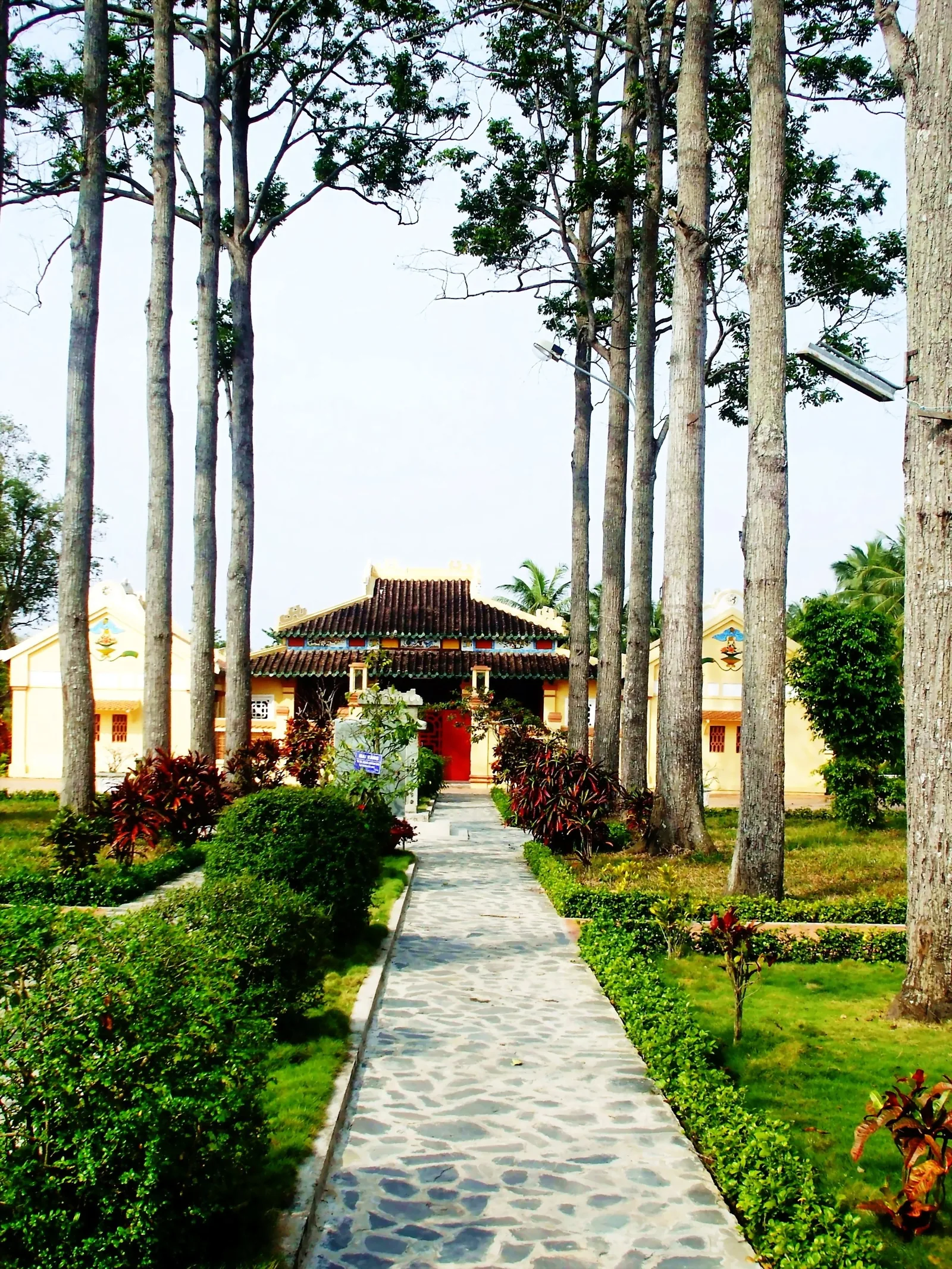 Con đường lát đá rợp bóng cây cao dẫn đến ngôi nhà cổ mái ngói đỏ tại Văn Thánh Miếu, Vĩnh Long.